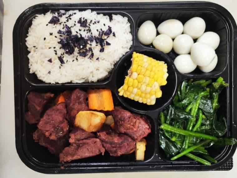 Bento box with rice, braised beef with potato and carrot, a segment of corn on the cob, quail eggs and sauteed leafy greens