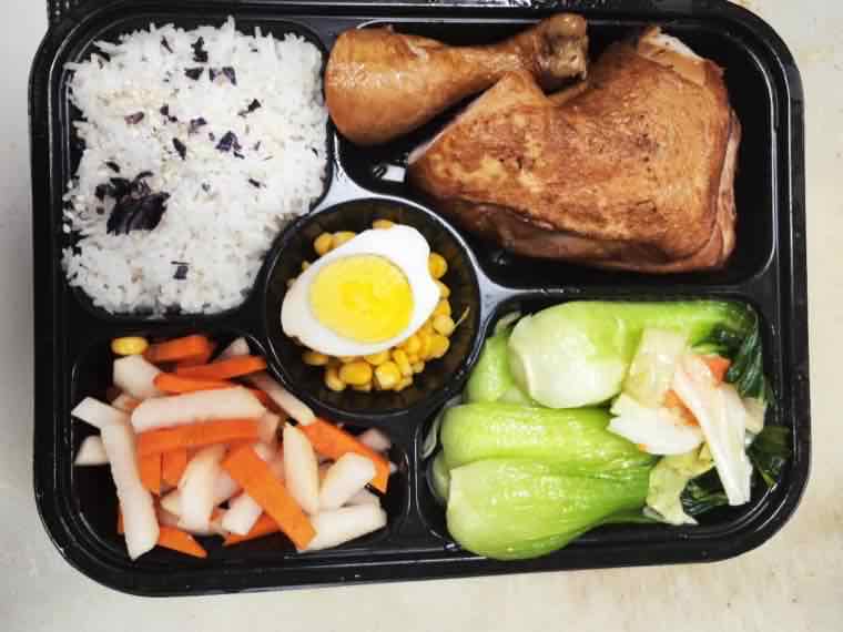 Five-compartment bento box with rice, a glazed roast chicken leg, a halved boiled egg on sweet corn, pickled carrot and daikon, and baby bok choy