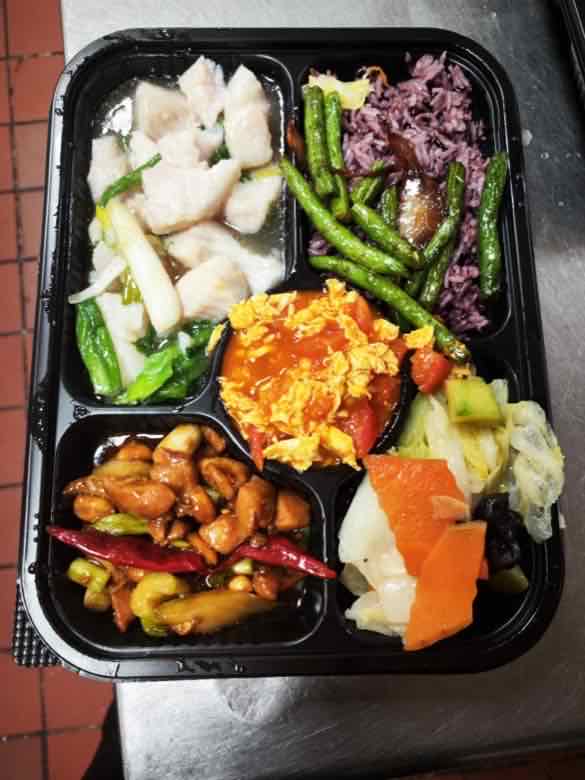 Bento box with steamed white fish fillet, purple rice, string beans, scrambled egg with tomato and Kung Pao chicken