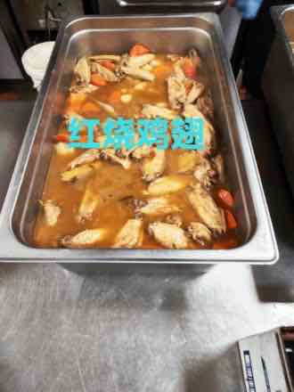Catering pan of braised chicken wings simmering with carrot chunks and ginger slices in a brown sauce