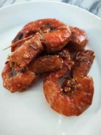 Braised shell-on shrimp White plate holding shell-on shrimp glazed in a glossy red-brown sauce with minced garlic