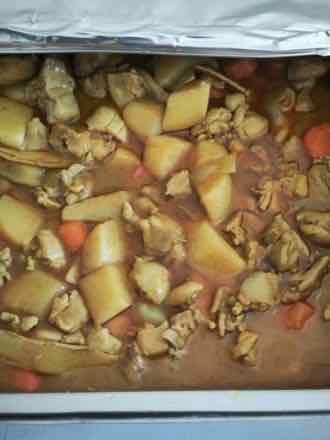 Catering tray of chicken chunks stewed with potato wedges and carrot pieces in a yellow-brown curry sauce