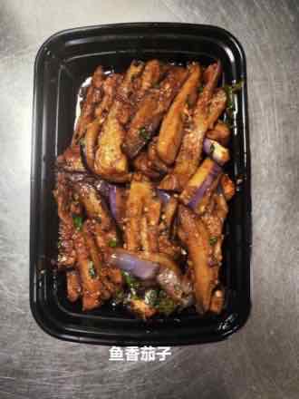 Tray of long-cut braised eggplant strips coated in a dark garlic chili sauce with minced garlic and chopped green herbs