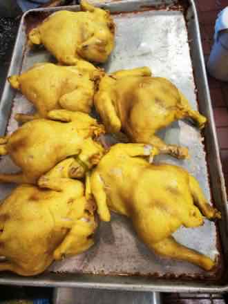 Whole poached chickens Sheet pan holding five whole cooked chickens with glossy yellow skin, prepared for slicing