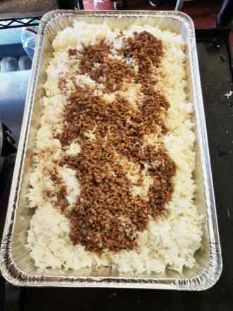 Large catering tray of steamed white rice topped down the center with browned seasoned minced meat