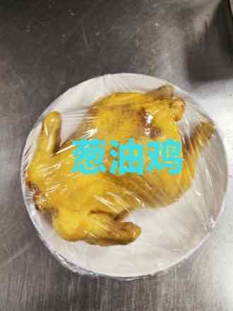 Whole cooked chicken with glossy yellow skin resting on a white plate on a stainless steel counter