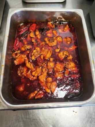 Pan of braised chicken pieces in a deep red chili oil sauce with whole dried red peppers