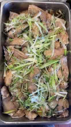Catering pan filled with lightly browned fish fillet pieces topped with shredded green onion and a light sauce