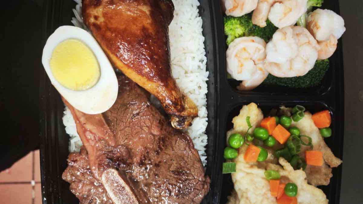 Topbento bento box Close-up of a Topbento bento box with a roast chicken leg, sliced beef, a halved boiled egg over white rice, shrimp with broccoli, and fish fillet with peas and carrot