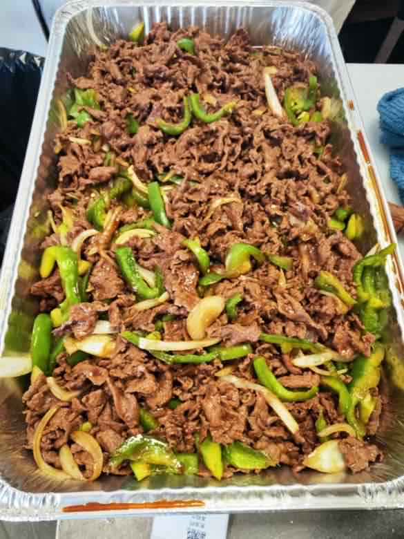 Large catering tray of sliced beef stir-fried with green bell pepper strips and onion in brown sauce