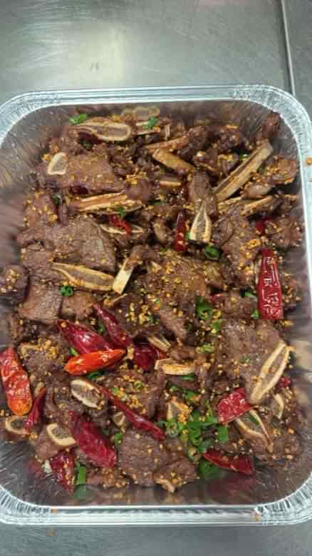 Catering tray of bone-in ribs with whole dried red chilies, toasted cumin seed and chopped scallion