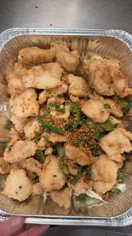 Catering tray of golden fried fish fillets over shredded cabbage with garlic, scallion and chopped jalapeno