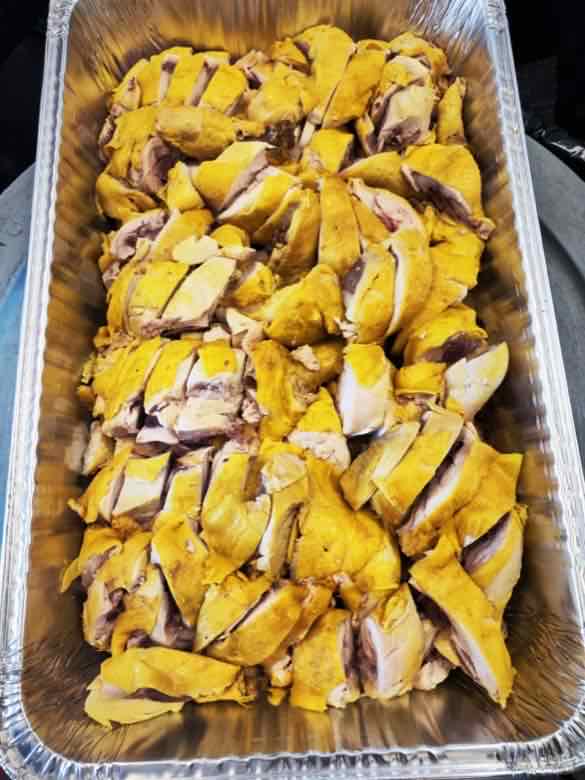 Catering tray neatly arranged with rows of chopped poached chicken pieces