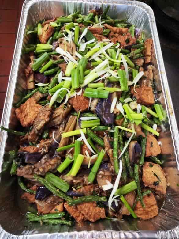 Catering tray of fried tofu braised with eggplant and green beans, topped with shredded scallion